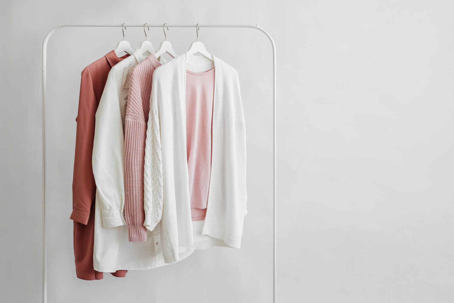 Feminine clothes in pastel pink color on hanger on white background. Elegant dress, jumper, shirt and other fashion outfit. Spring cleaning home wardrobe. Minimal concept.